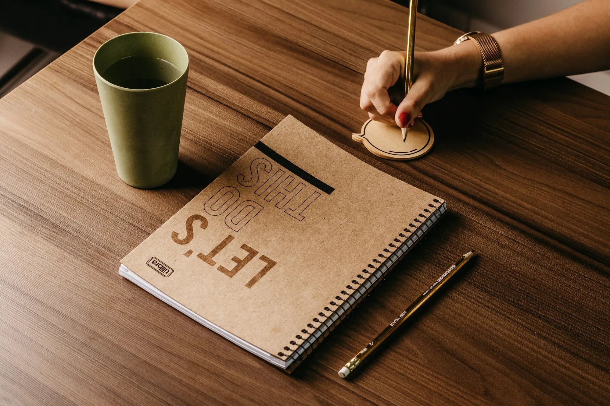 Somebody writing in a notebook beside a cup of coffee